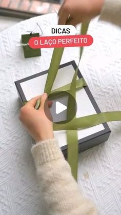 a person is holding a green ribbon on a piece of paper and cutting it with scissors