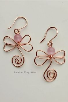 two earrings with pink beads on them and wire wrapped around the ear wires, sitting on top of a white surface