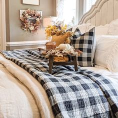 a bed with plaid blankets and pillows on it in front of a window, next to a table with pumpkins