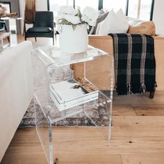 a clear acrylic side table with books on it in front of a couch