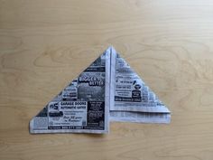 an origami piece of newspaper folded in the shape of a triangle on top of a wooden table