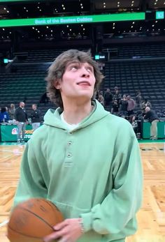 a young man holding a basketball on top of a wooden floor in front of an arena