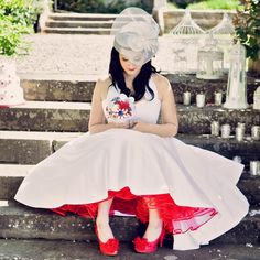 a woman sitting on the steps wearing red shoes and a white dress with flowers in her hair