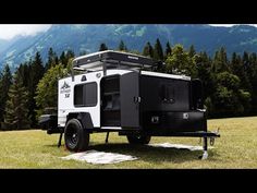 an off - road camper parked in the middle of a field with mountains in the background