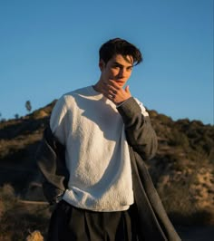 a young man is standing in the desert with his hand on his face and looking off into the distance