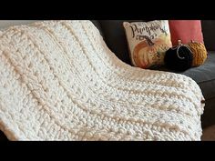 a white crocheted blanket sitting on top of a couch next to a pillow