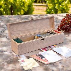 an open wooden box sitting on top of a table next to some grapes and papers