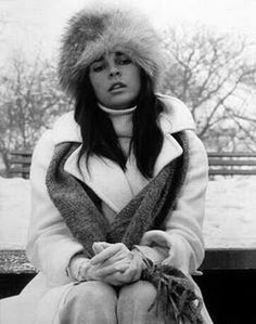 black and white photograph of a woman sitting on a bench in the snow wearing a fur hat