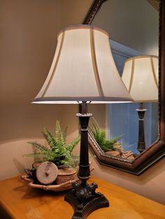 a lamp sitting on top of a wooden table next to a mirror and potted plant