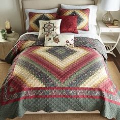 a bed covered in a multi colored quilt and pillows next to a night stand with two lamps