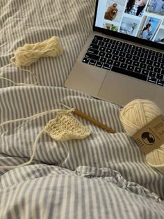 an open laptop computer sitting on top of a bed next to two balls of yarn