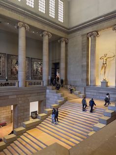 several people are walking up and down the stairs in a building with paintings on the walls