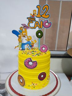 a yellow birthday cake with donuts and sprinkles on the bottom tier