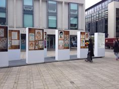 some people are walking around in front of an art exhibit on the sidewalk near a building