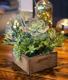 a wooden box filled with succulents on top of a table next to candles