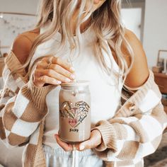 a woman holding a jar of coffee in her hands and wearing a cardigan sweater