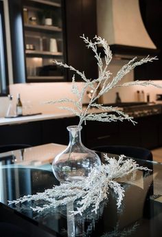 a glass table topped with a vase filled with water and branches on top of it