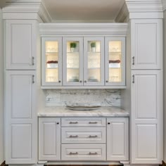 a white kitchen with marble counter tops and cabinets in the corner, along with hardwood floors