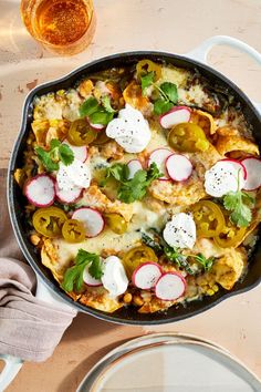 a skillet filled with vegetables and cheese on top of a table next to plates