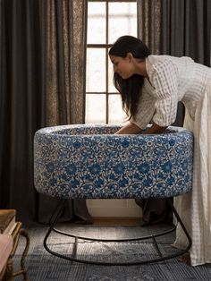 a woman bending over on top of a blue ottoman in front of a window with curtains