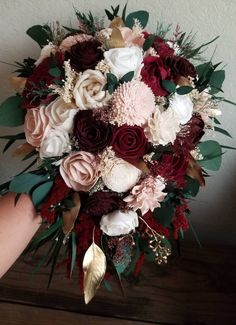 a bridal bouquet with red, white and pink flowers on the bottom is being held by someone's hand