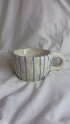 a blue and white striped cup sitting on top of a white cloth covered tablecloth