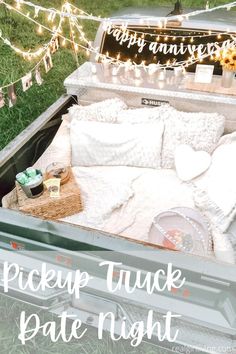 an open truck bed with white pillows and blankets in the back is surrounded by string lights