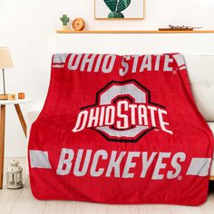 a red blanket with the word ohio state on it in front of a white couch