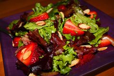 a salad with strawberries and almonds on it sitting on a purple square plate