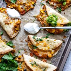 several quesadillas on a baking sheet with sour cream and cilantro