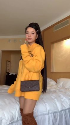 a woman standing in front of a bed wearing boots and a yellow sweater over her head