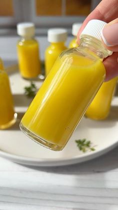 a person is holding a jar with yellow liquid in it and some small jars behind them