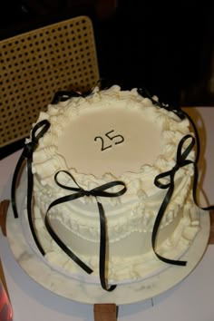 a white cake with black ribbon and the number 25 on it sitting on a table