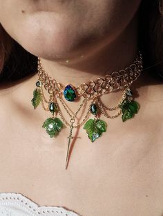 Behold the elegance of this gold-hued chainmail necklace! A vivid green rhinestone steals the spotlight at the heart, while a dangling sword charm and cascading layers of chains adorned with green teardrop beads and delicate ivy leaves add a touch of enchantment. Fit for a fairy warrior queen, this unique statement piece is destined to captivate. Actual colors of any item or chains may slightly differ from screen to screen due to the screen resolution. I take our pictures in natural light during Green Shoulder Jewelry, Luxury Medieval Metal Jewelry, Medieval Jewelry Emerald, Cheap Green Nature-inspired Jewelry, Cheap Green Choker As Gift, Cheap Green Choker As A Gift, Green Fairytale Accessories, Luxury Green Jewelry Sets For Festivals, Cheap Green Trendy Choker