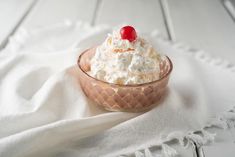 a small bowl filled with whipped cream and a cherry on top, sitting on a white cloth