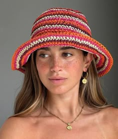 a woman wearing a multicolored hat with gold earrings on her left ear and chest