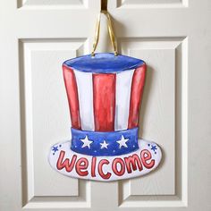 a welcome sign hanging on a door with an american hat painted on it's side