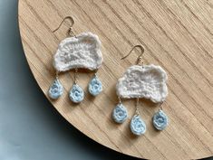 three crocheted earrings with dangling drops on top of a wooden table next to a clock