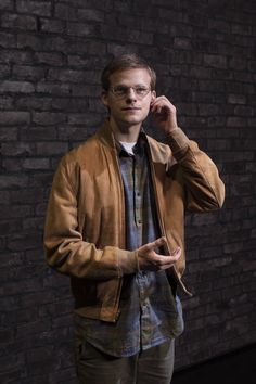 a man standing in front of a brick wall talking on a cell phone and holding his hand to his ear