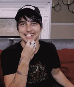 a young man sitting on top of a couch wearing a baseball cap and diamond ring