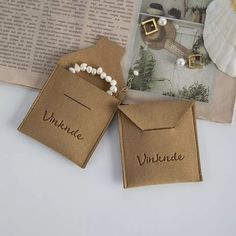 two brown tags with white pearls are sitting next to an open book and some other items