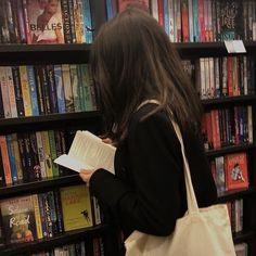 a woman standing in front of a bookshelf holding a book and looking at it