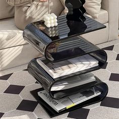 a woman sitting on a couch next to a table that has magazines stacked on it