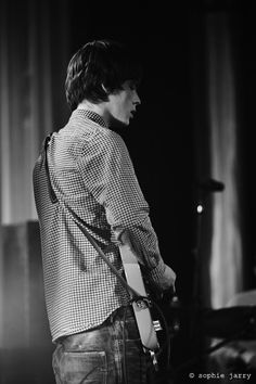 a man standing in front of a microphone on stage with his guitar strapped to his back