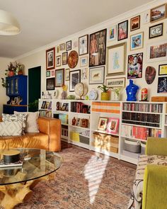 a living room filled with furniture and lots of pictures on the wall above it's glass coffee table