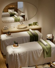 two beds in a room with white sheets and green towels on them, near a mirror