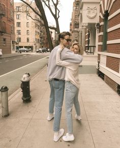 two people are hugging on the sidewalk near a fire hydrant and building in the background