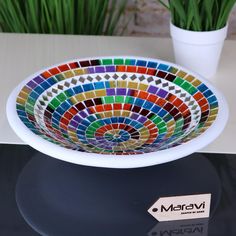 a colorful bowl sitting on top of a table next to a potted green plant