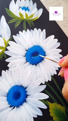 someone is painting flowers with acrylic paint on a black sheet that has white and blue flowers painted on it