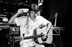 a man holding a guitar and drinking from a cup while sitting in front of a microphone